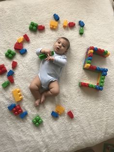 a baby laying on top of a white blanket next to toy blocks and letters that spell out the word e