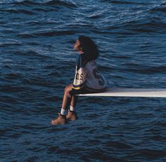 a woman sitting on the edge of a boat in the ocean looking up at the sky