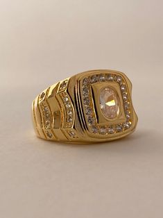 The Varsity Ring is a bold bruiser! This stylish piece is the perfect gold statement ring for men that can be worn by women too, as an oversized boyfriend ring! This cool ring features a square face with a central brilliant cut cubic zirconia stone framed by micro pave stones and a CZ encrusted wide band. Available in 24K gold or rhodium plating over steel Patent plating & sealant technology to ensure durability and long lasting wear Made in Los Angeles, CA | Nickel & Lead Free Boys Gold Ring, Boyfriend Ring, Ring For Boyfriend, Cool Ring, Square Face, Gold Statement Ring, Square Faces, Ring For Men, Cz Ring