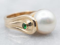 "This gorgeous modernist piece is crafted of polished yellow gold that is polished to a perfect shine. Utterly sleek, this vintage piece features a single, luscious pearl accented by sparkling diopside gemstones! Metal: 14K Yellow Gold Gem: Pearl Gem Measurements: 10.5 mm, Round Accents: 2 Diopside totaling .08 Carats Ring Size: 4.25 Marks: \"14K\" Stamped on the inside band SKU #: A27004 Each piece has been identified and graded by a Graduate Gemologist who has been certified by the Gemological Institute of America (GIA). We have six brick-and-mortar storefronts in Maine, Massachusetts, and New Hampshire and have been in business for over 25 years! Please visit our Shop's About Page or our website for more information about our jewelry. For questions about diamond grading, we recommend th Elegant Green Pearl Ring With Gemstone, Elegant Tsavorite Rings With Polished Finish, Elegant Green Gemstone Pearl Ring, Gold Pearl Ring With Polished Finish, Classic Multi-stone Pearl Ring For Formal Occasions, 14k Gold Pearl Ring With Polished Finish, Luxury 14k Gold Pearl Ring With Polished Finish, Luxury Yellow Gold Pearl Ring With Cabochon, Gold Pearl Ring