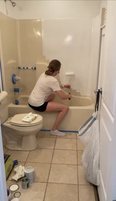 a woman is sitting on the edge of a bathtub while cleaning it with a rag