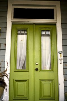 a green front door with two sidelights and curtains on the top half of it