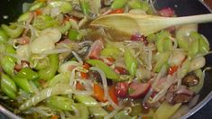 a pan filled with vegetables and meat on top of a stove next to a wooden spoon