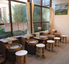 a room filled with lots of wooden stools and tables next to large windows on the wall