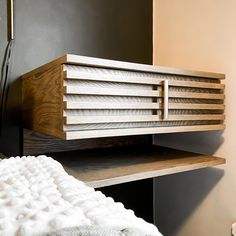 a bed with a wooden headboard and white blanket on it next to a black wall