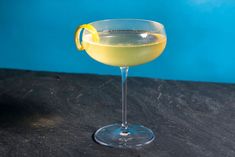 a glass filled with yellow liquid on top of a black table next to a blue wall