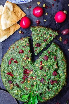 a pizza with spinach and cranberries on it next to pita bread