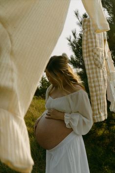 a pregnant woman standing next to clothes hanging on a line