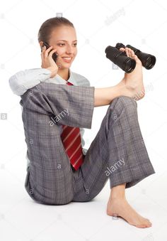 a woman in business attire sitting on the floor talking on her cell phone and holding binoculars - stock image