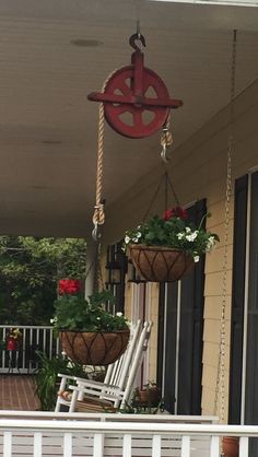 two hanging planters with flowers on the front porch, one holding a rocking chair