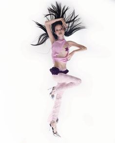 a woman in pink shirt and black pants dancing with her hair flying through the air