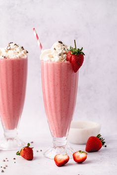 two strawberry milkshakes with whipped cream and strawberries on the side, sitting next to each other