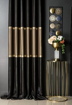 a black and gold curtain in front of a vase with flowers on it next to a mirror