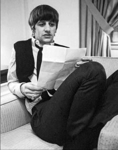 a man sitting on top of a couch holding a paper in his hand and looking at the camera