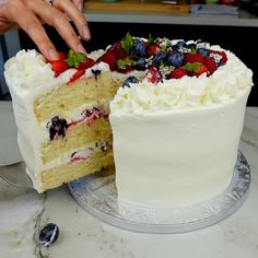 a person is cutting into a cake with white frosting and berries on the top