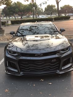 a black sports car parked in a parking lot next to a curb with trees on it