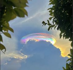 a rainbow colored cloud in the sky with trees and clouds behind it, as seen from below