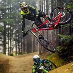 a man riding on the back of a red bike over a dirt hill next to another person