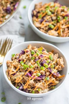 three white bowls filled with coleslaw, carrots and green onions next to a gold fork