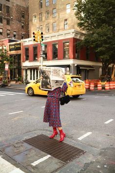 a woman standing on the side of a street holding up a newspaper over her head