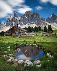 a small pond in the middle of a grassy field with mountains in the back ground