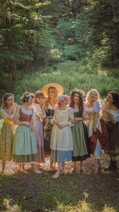 a group of young women standing next to each other on a forest trail wearing dresses and bonnets