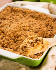 a close up of a wooden spoon with food in a casserole dish on a table