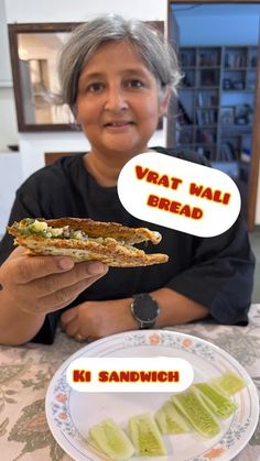 a woman sitting at a table with a sandwich and pickles in front of her