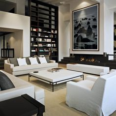 a living room filled with white couches and chairs next to a book shelf full of books