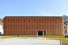 two people walking in front of a building with wooden panels on the side and green grass