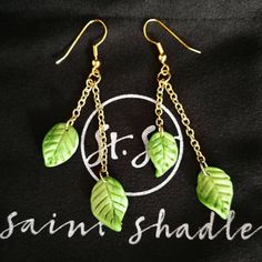 three green leaves hanging from gold chains on a black t - shirt with the words saint shade