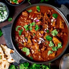 a bowl filled with meat and vegetables next to pita bread, cilantro