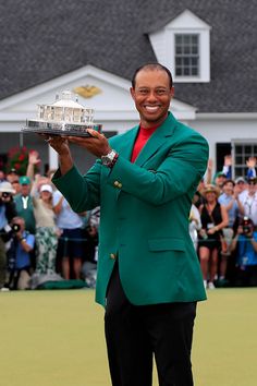 a man in a green jacket holding up a trophy on top of a golf course