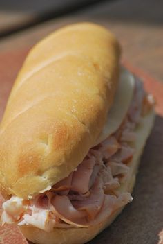 a sub sandwich with meat and cheese on a wooden table next to slices of grapefruit