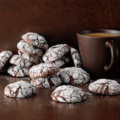 a pile of powdered sugar cookies next to a cup of coffee on a table