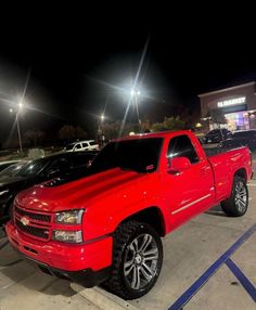 a red pickup truck parked in a parking lot at night with other cars behind it