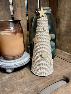 a small white christmas tree next to a lit candle on a wooden table with other items in the background