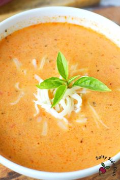 a white bowl filled with soup and garnished with cheese, on top of a wooden table