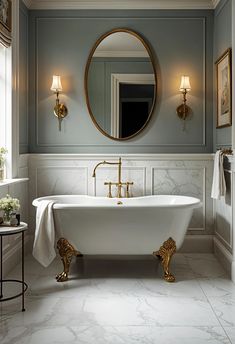 a white bath tub sitting under a bathroom mirror next to a table with a lamp on it