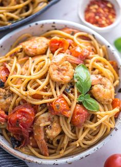 pasta with shrimp, tomatoes and basil in a white bowl on top of a table