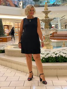 a woman standing in front of a fountain wearing black heels and a dress with ruffles