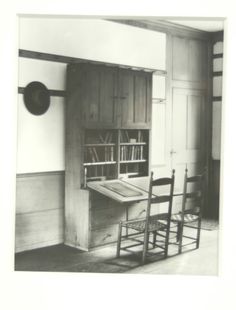 an old black and white photo of a desk with bookshelf in the background