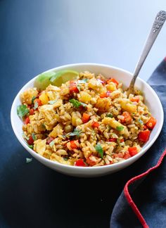 a bowl filled with rice and vegetables on top of a blue cloth next to a spoon