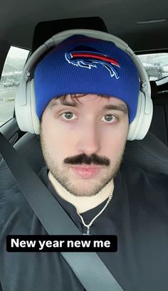 a man wearing headphones and a blue beanie is sitting in the back seat of a car