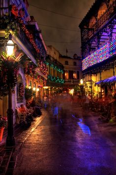 people walking down the street at night with christmas lights on buildings in the back ground