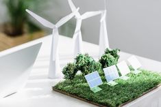 three wind turbines on top of a green field with trees and grass in the foreground