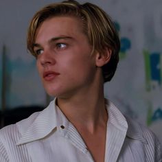 a young man with blonde hair and blue eyes stares into the distance while wearing a white shirt