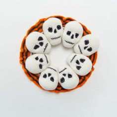 six crocheted skulls are arranged in a circle on an orange and white background