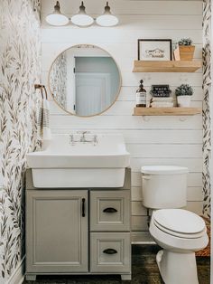 a white toilet sitting next to a bathroom sink under a mirror and light above it