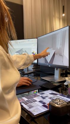 a woman pointing at two computer screens on a desk